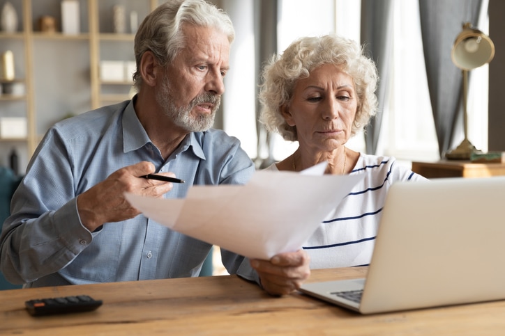 Stressed elderly married couple sitting at table at home manage budget having financial problems with their utility bills