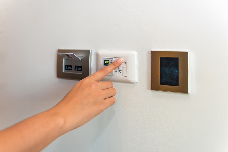 A person adjusting their thermostat.