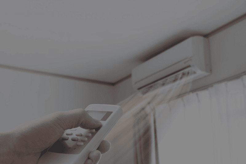 A person holding a remote, aimed at a ductless unit to turn it on.
